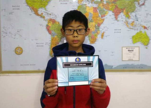 A boy holding up his certificate for completing an english course.